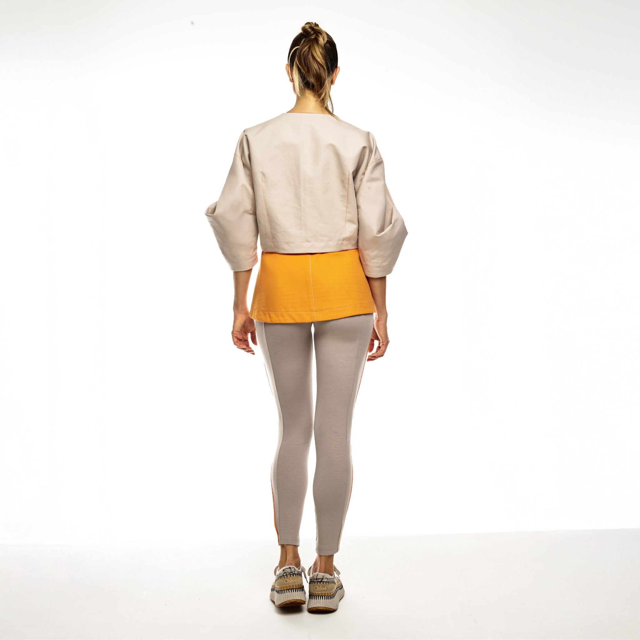 Person wearing a beige/orange jacket and beige jumpsuit on a white background
