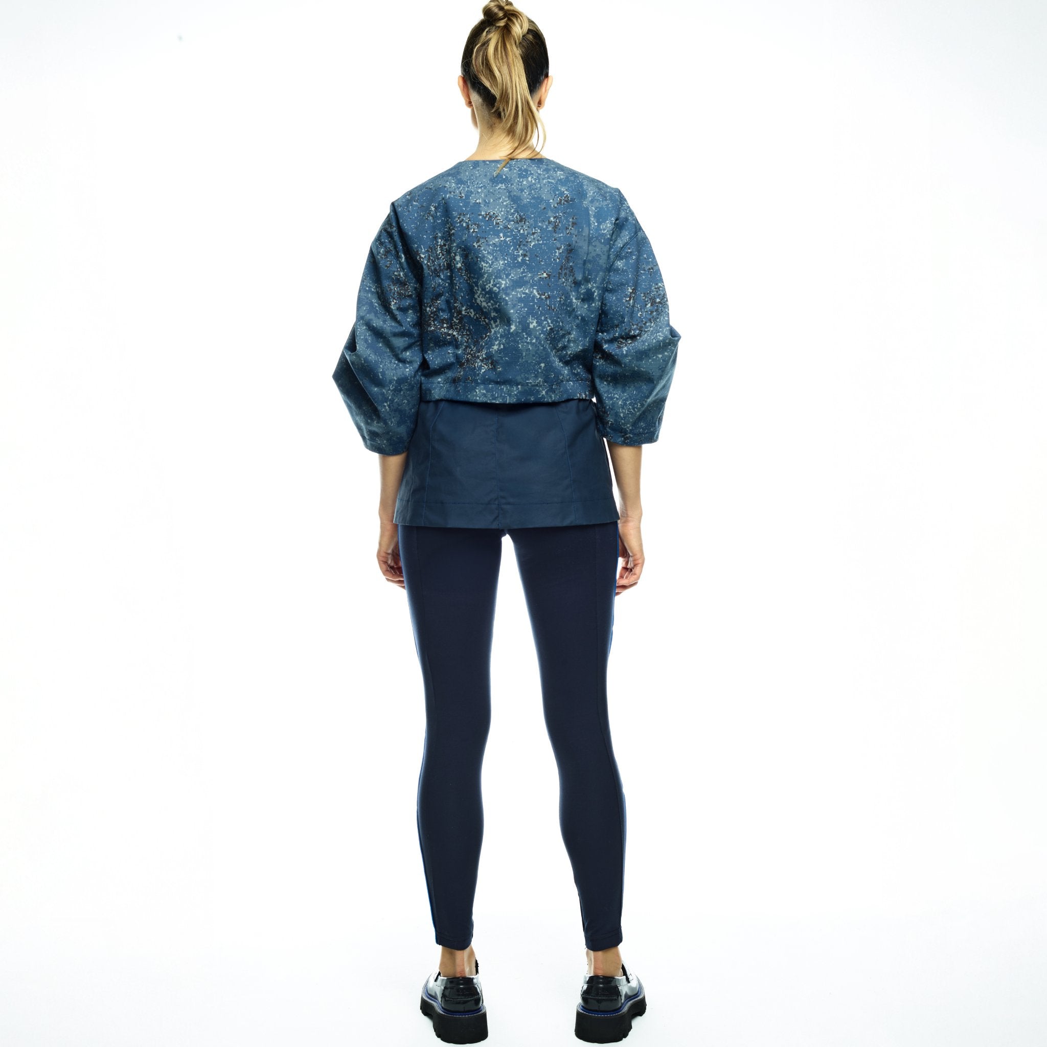 Person wearing a blue patterned jacket and dark leggings on a white background