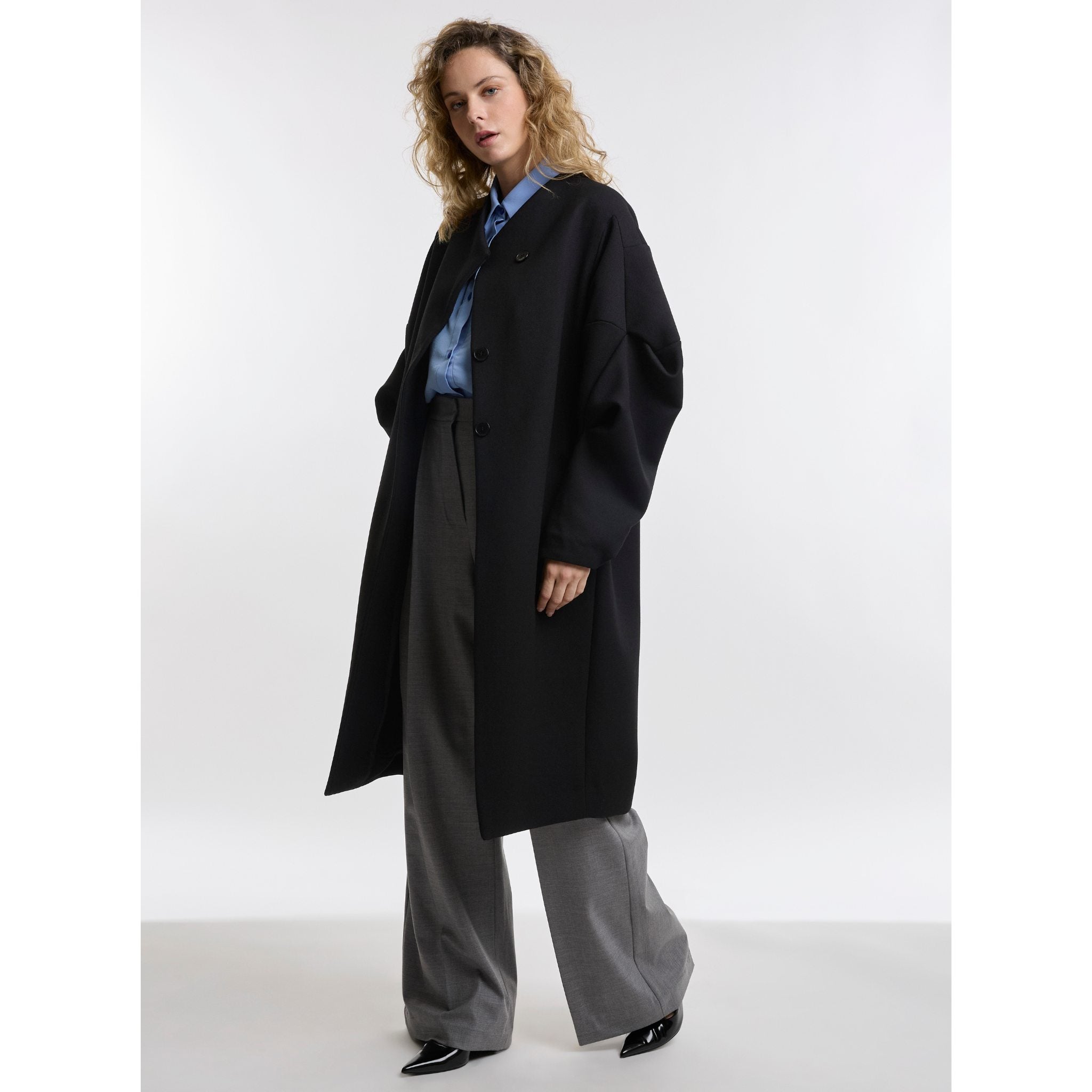 Woman wearing black coat with grey trousers on white background