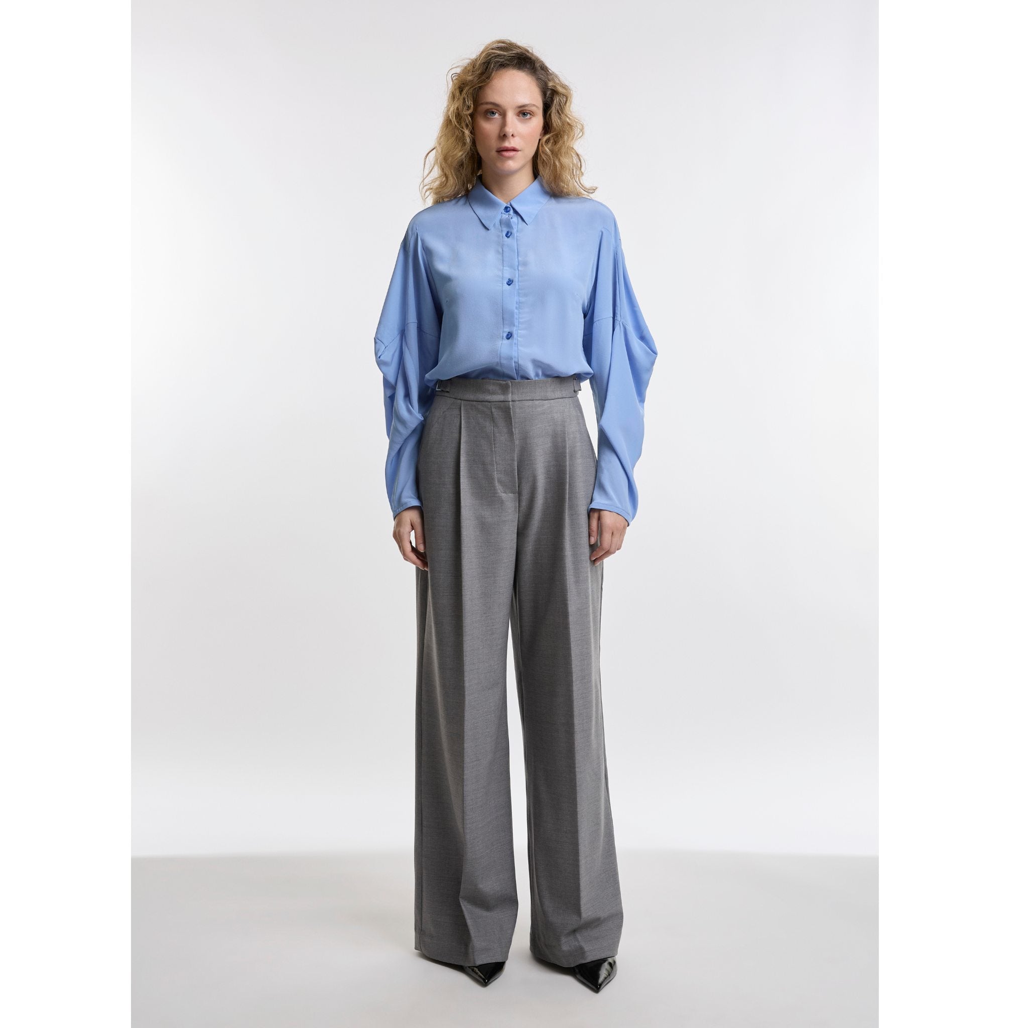 Woman wearing a light blue shirt and gray pants on a white background