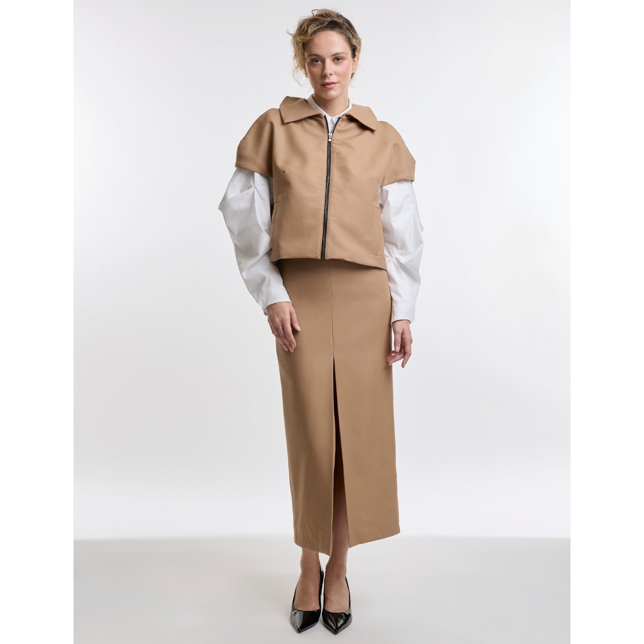 Woman wearing a camel jacket and skirt with a white shirt on a white background