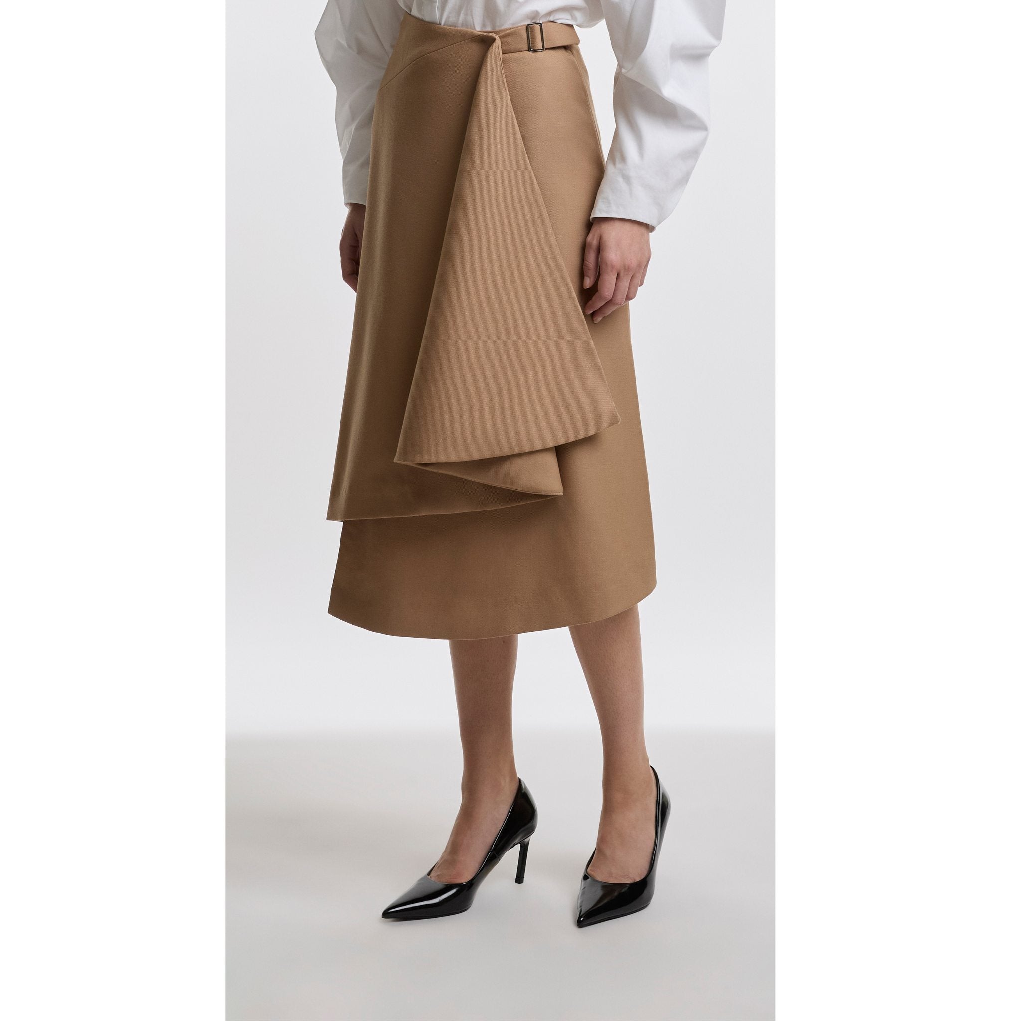 Person wearing a camel layered skirt with a white shirt on a light grey background