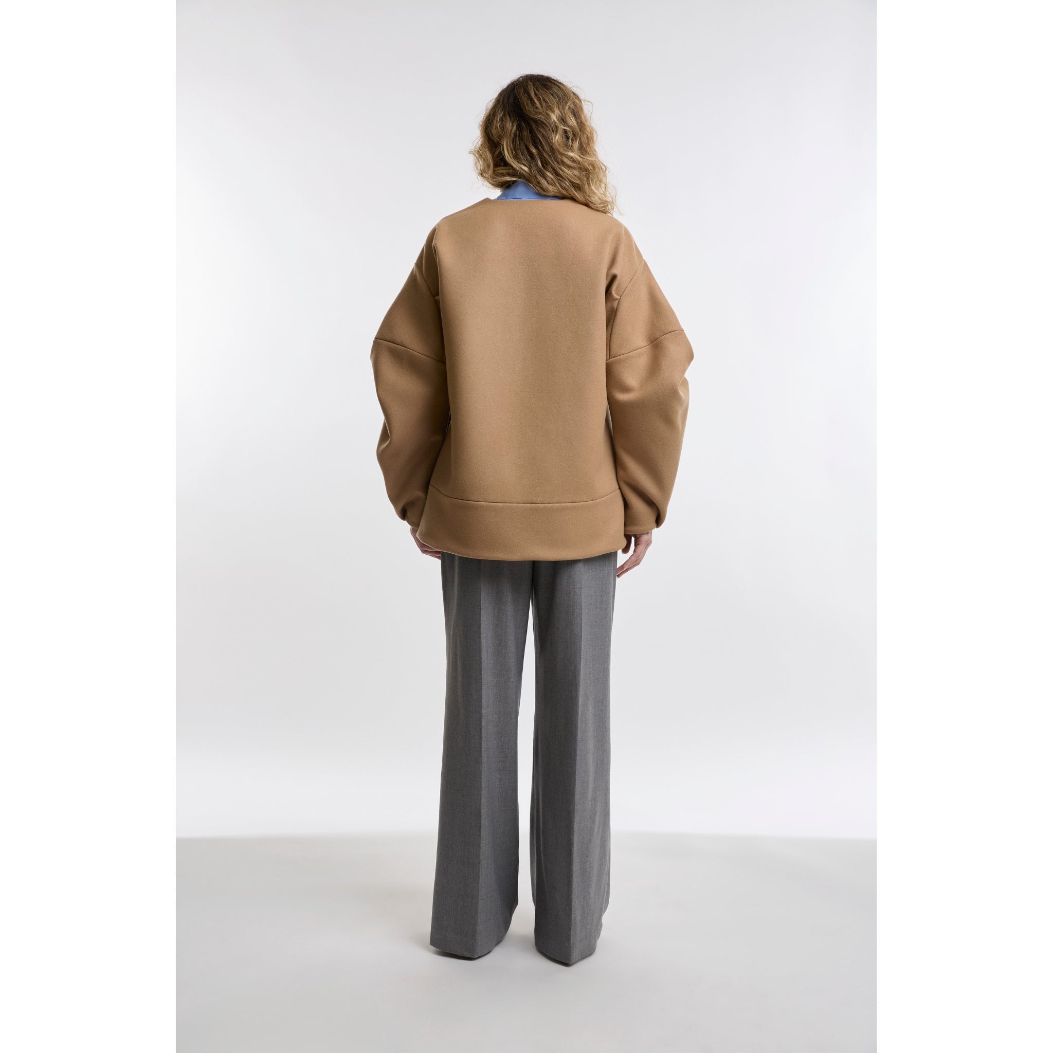 Person wearing a camel jacket and grey pants on a white background