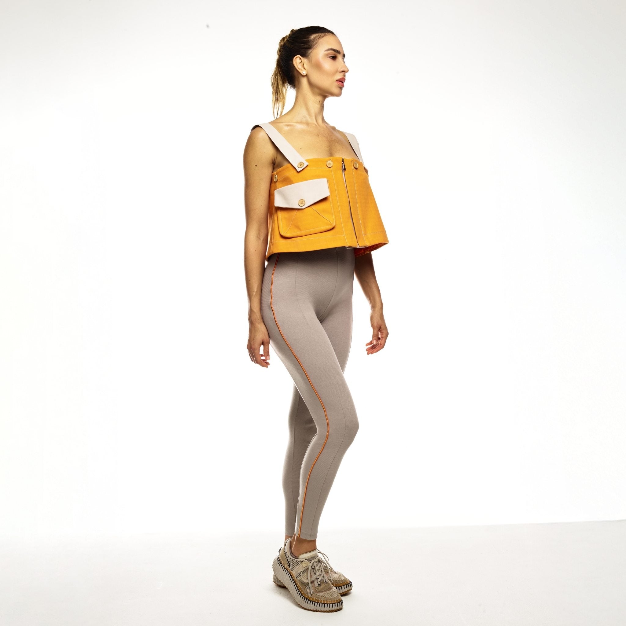 Woman wearing an orange top and beige jumpsuit on a white background