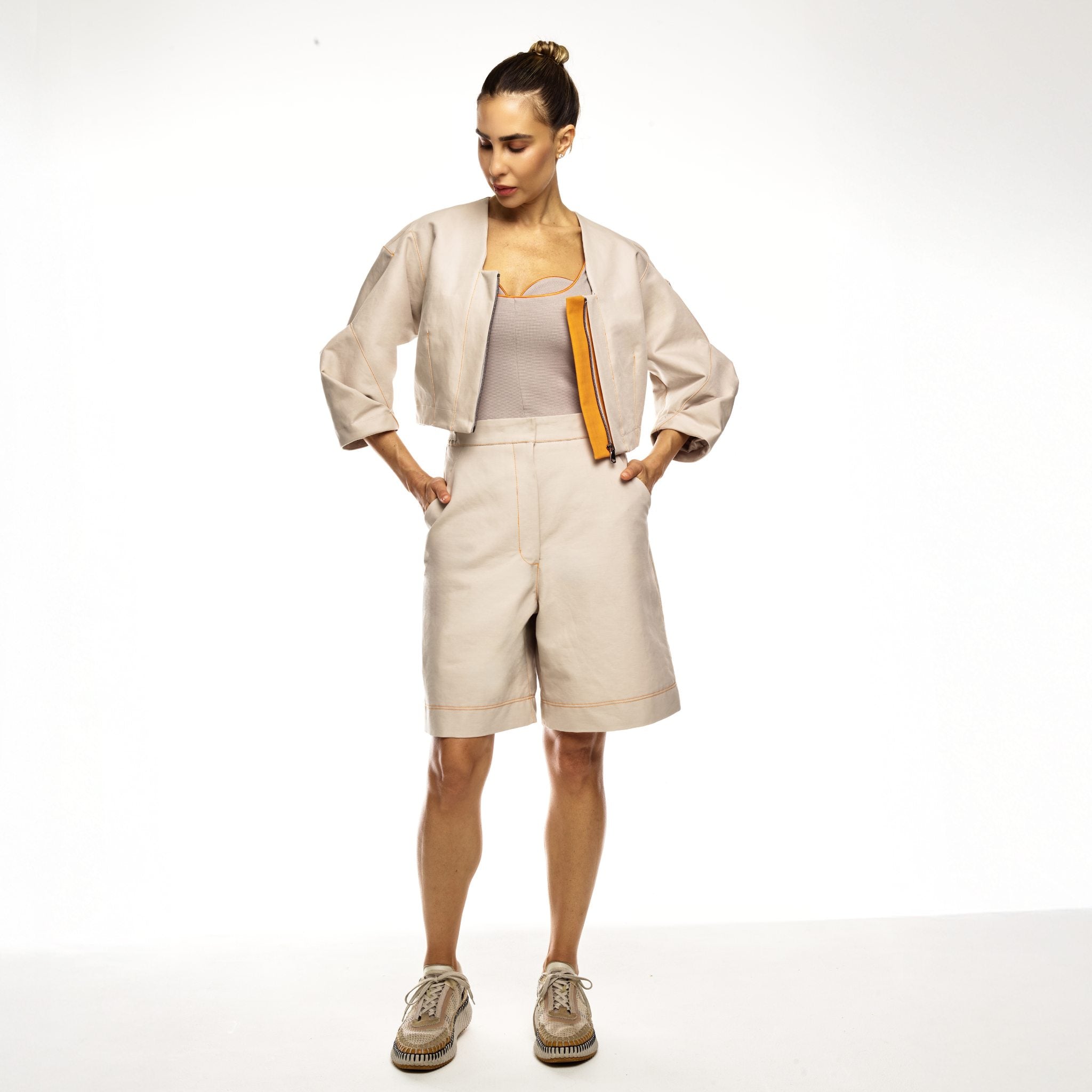 Woman wearing a beige outfit with shorts and a jacket on a white background