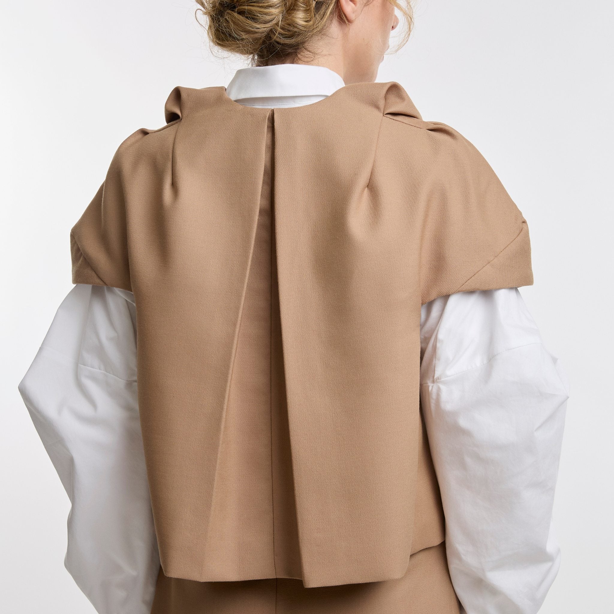 Person wearing a camel jacket over a white shirt on a white background