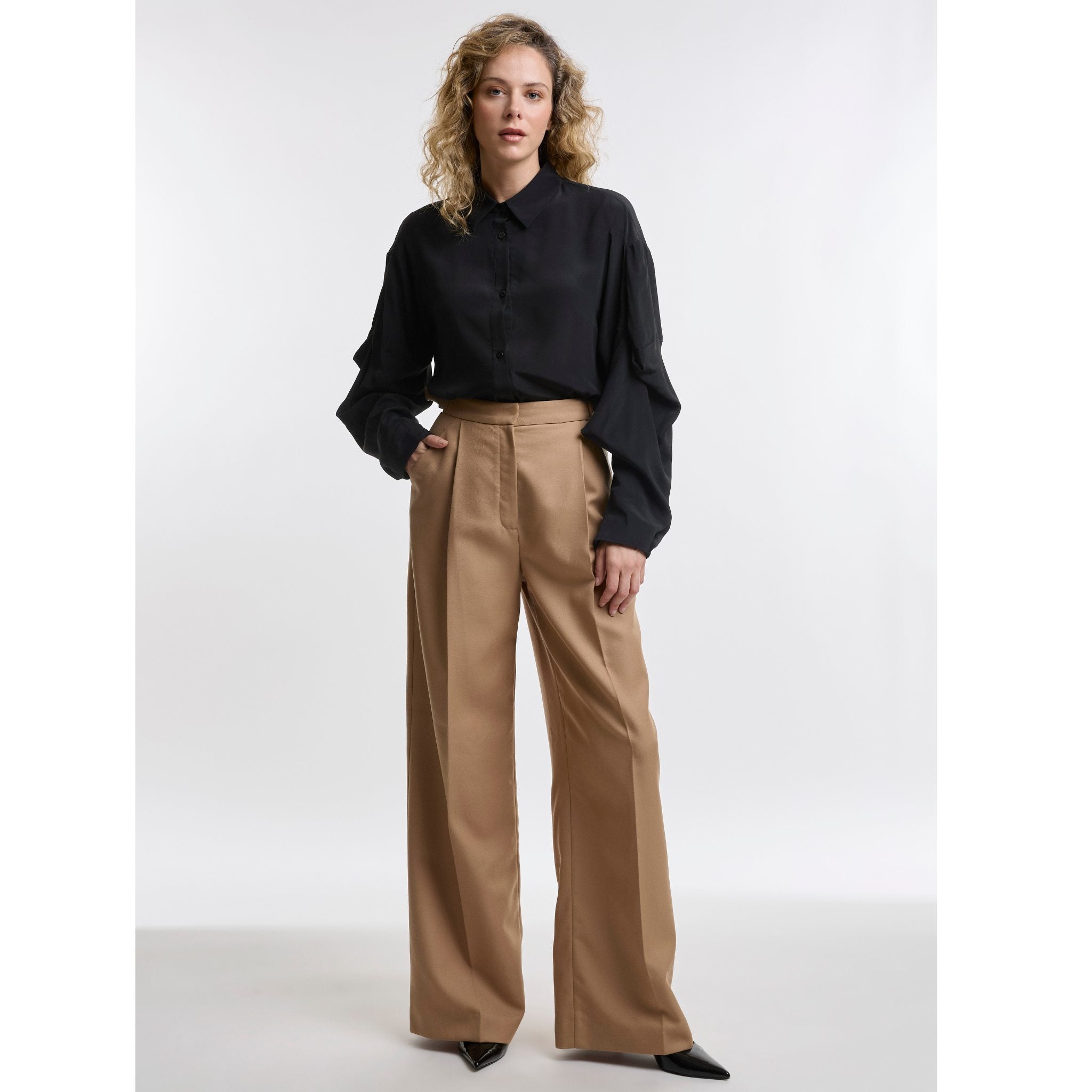 Woman wearing a black blouse and camel pants on a white background