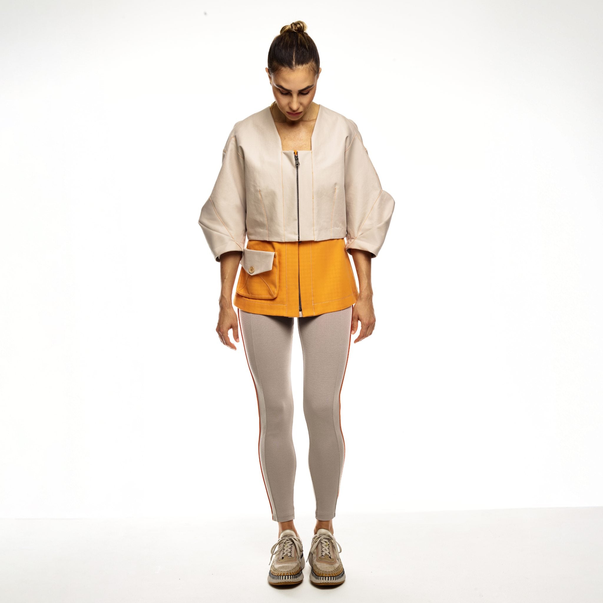 Woman wearing a beige and orange jacket with beige jumpsuit on a white background