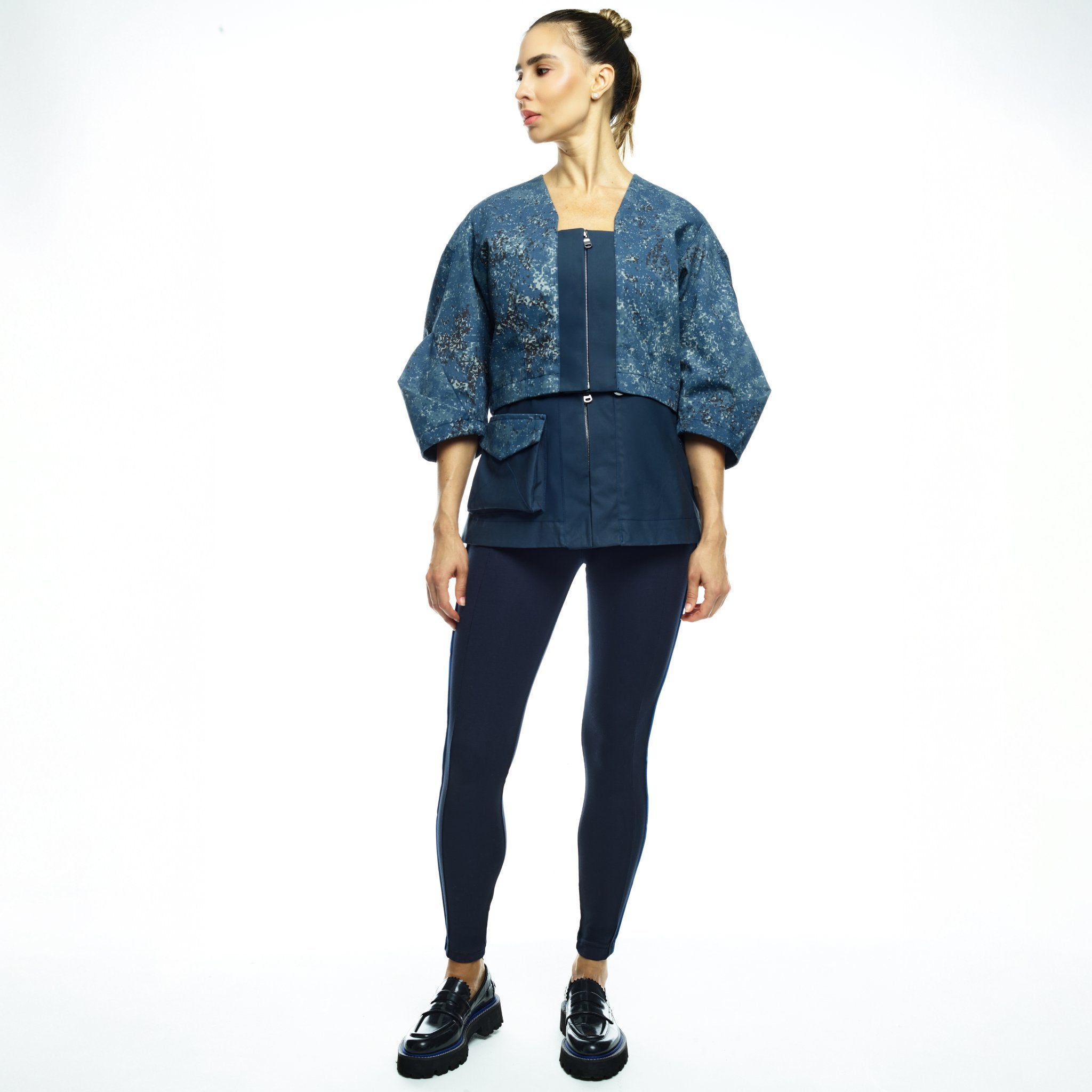 Woman wearing a blue jacket and dark jumpsuit on a white background