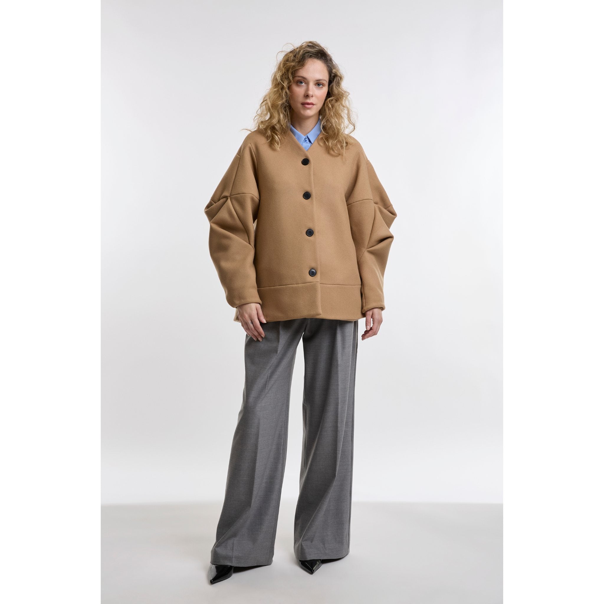 Woman wearing a camel jacket and grey pants on a white background