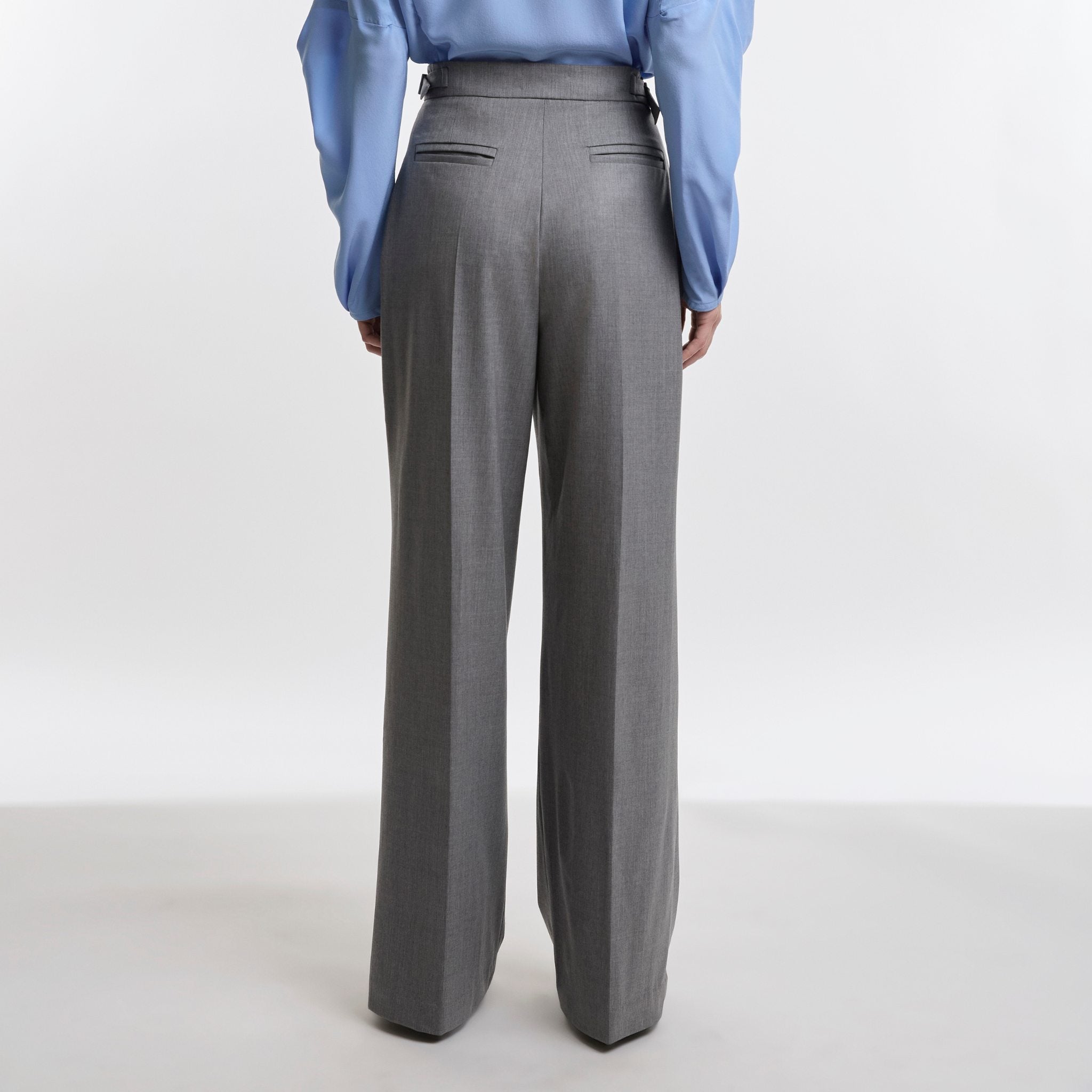 Person wearing gray high-waisted pants with a blue shirt on a white background