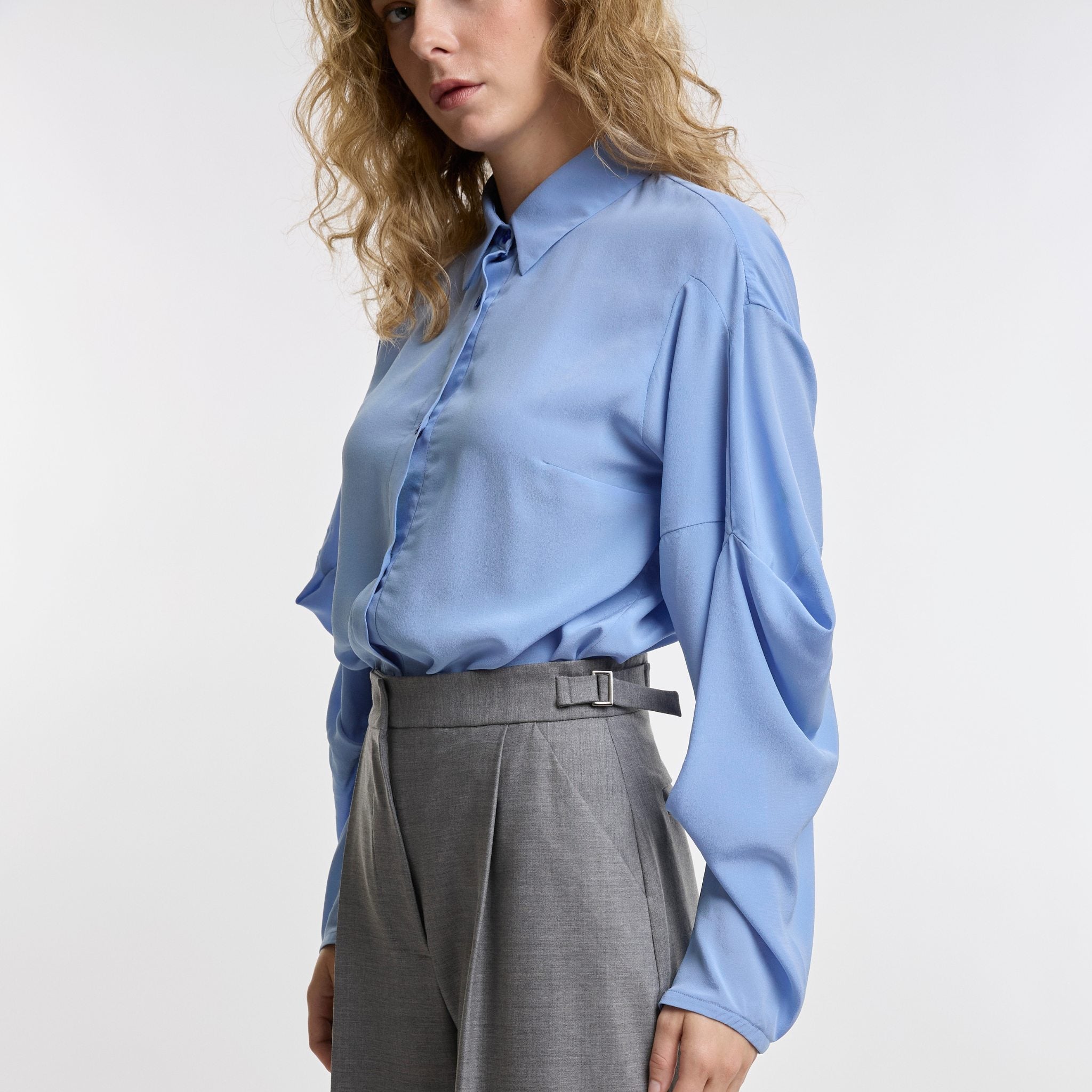 Woman wearing a light blue shirt and gray pants on a white background