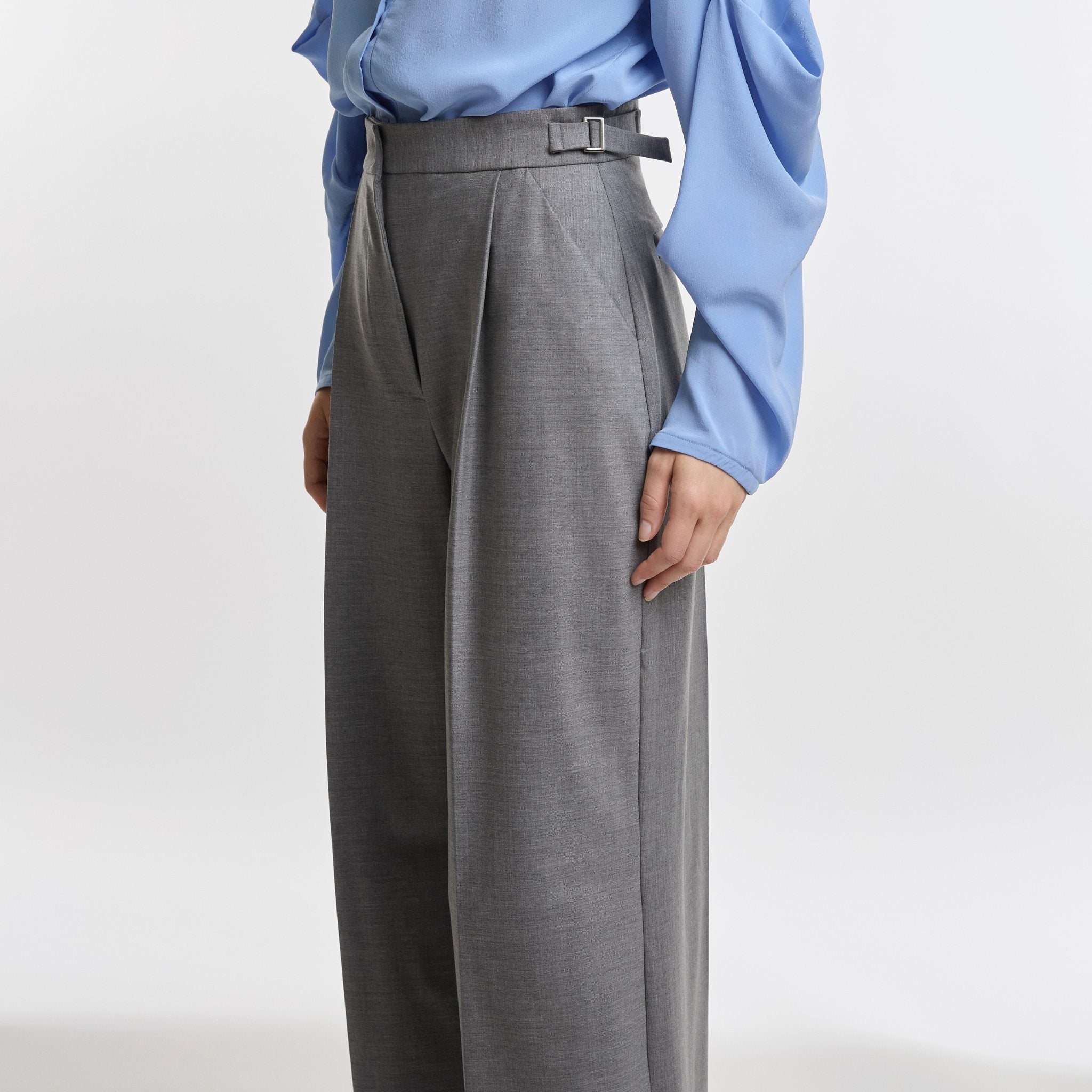 Person wearing a light blue shirt and gray wide-leg pants on a white background